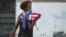 Una mujer con una máscara protectora contra el coronavirus y una bandera de EEUU camina por una calle de La Habana. (Yamil Lage/AFP)