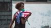 Una mujer con una máscara protectora contra el coronavirus y una bandera de EEUU camina por una calle de La Habana. (Yamil Lage/AFP)