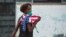 Una mujer con una máscara protectora contra el coronavirus y una bandera de EEUU camina por una calle de La Habana. (Yamil Lage/AFP)