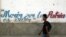 Un joven camina junto a un muro con un frangmento del himno nacional de Cuba. 
