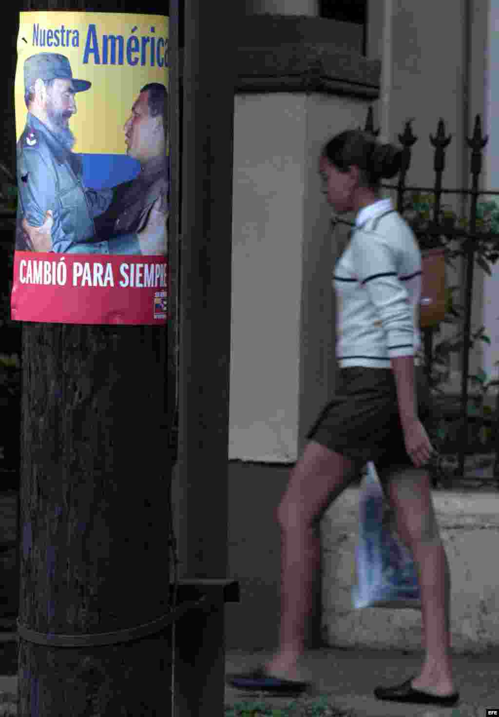 Una mujer barre la calle frente a un cartel del ALBA.
