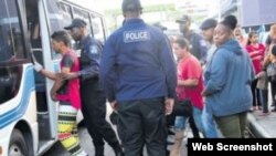 Miembros de la Unidad de Protección de menores trasladan a los cubanos que estaban acampados junto a sus padres en Port-of-Spain. Foto Guardian.