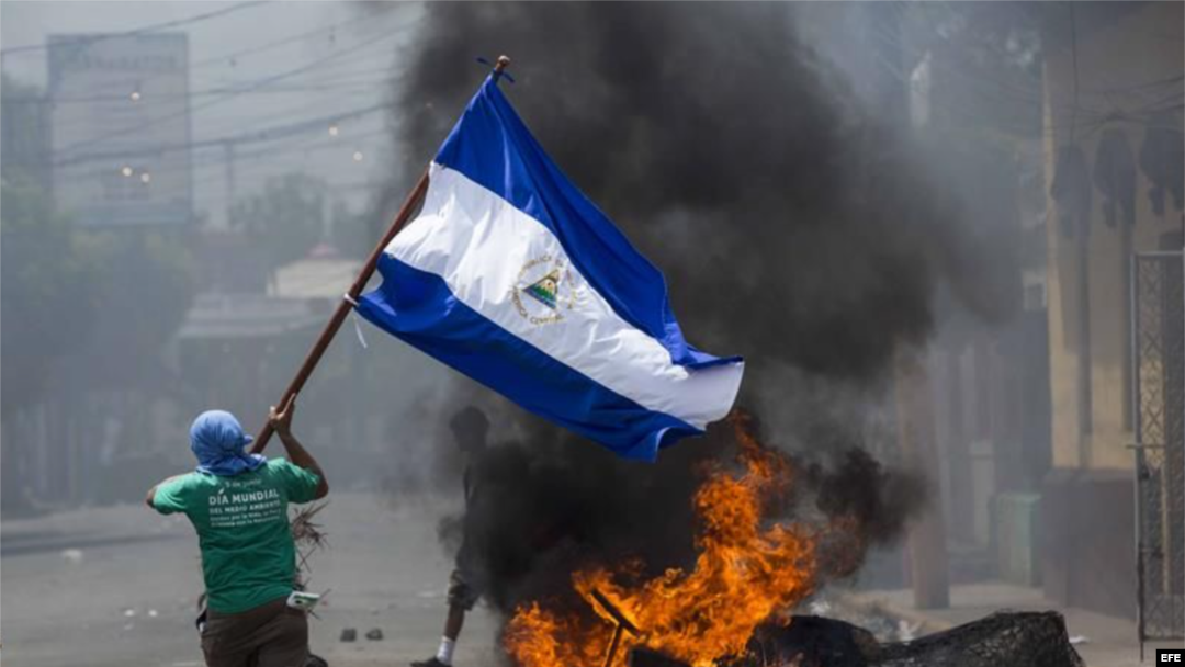 Un joven corre con la bandera de Nicaragua frente a unas llantas incendiadas ayer en la ciudad de Masaya (Nicaragua). EFE