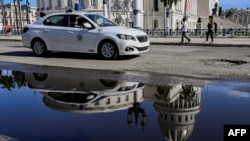 Un vehículo policial patrulla una calle de La Habana, con el Capitolio de fondo reflejándose cabeza abajo en un charco de agua. 