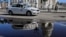 Un vehículo policial patrulla una calle de La Habana, con el Capitolio de fondo reflejándose cabeza abajo en un charco de agua. 