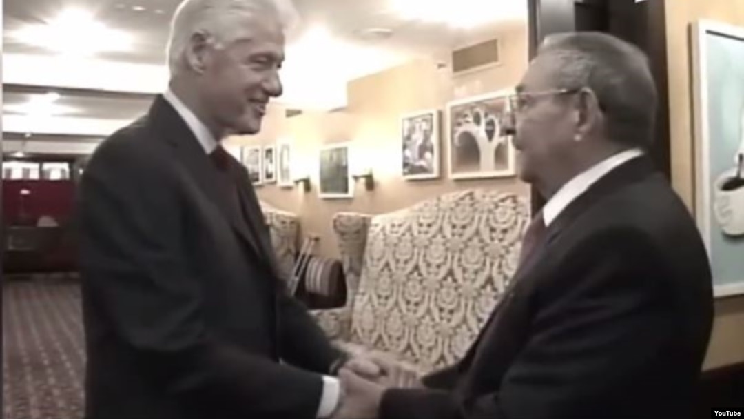 Bill Clinton y Raúl Castro se toman efusivamente de las manos.
