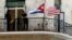  Dos jóvenes cubanos conversan junto a las banderas de Estados Unidos y Cuba.