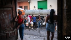 Residentes transportan recipientes mientras hacen fila para obtener agua potable de un camión cisterna, en Matanzas, Cuba.